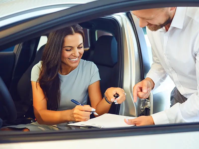 Woman in car signing auto loan papers held by lender